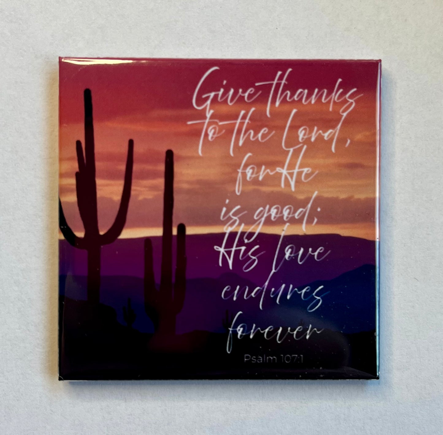Christian scripture magnet with desert sunset and saguaro silhouettes featuring Psalm 107:1 about giving thanks to the Lord