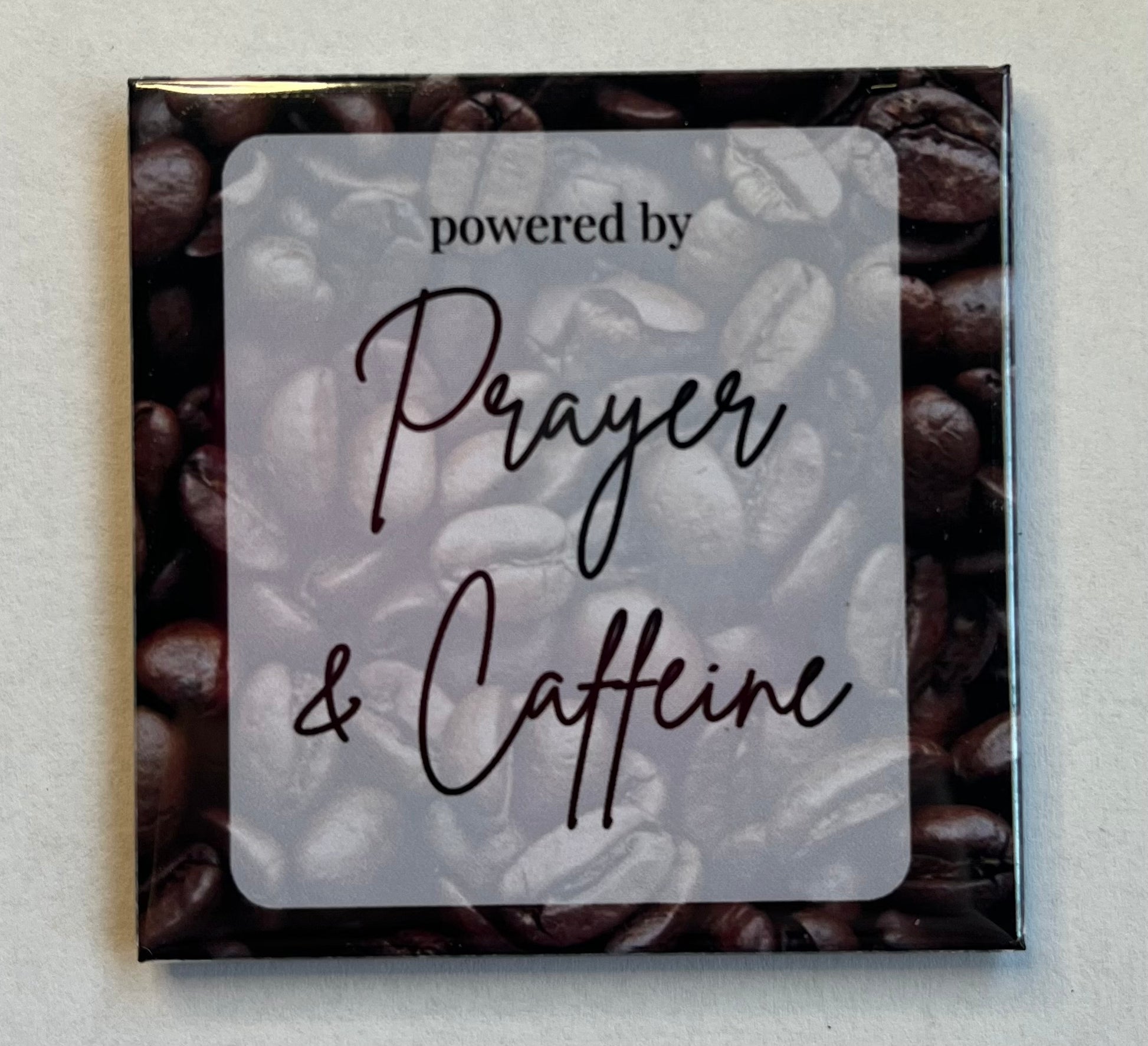 Faith-based coffee magnet with coffee beans background reading Powered by Coffee and Prayer