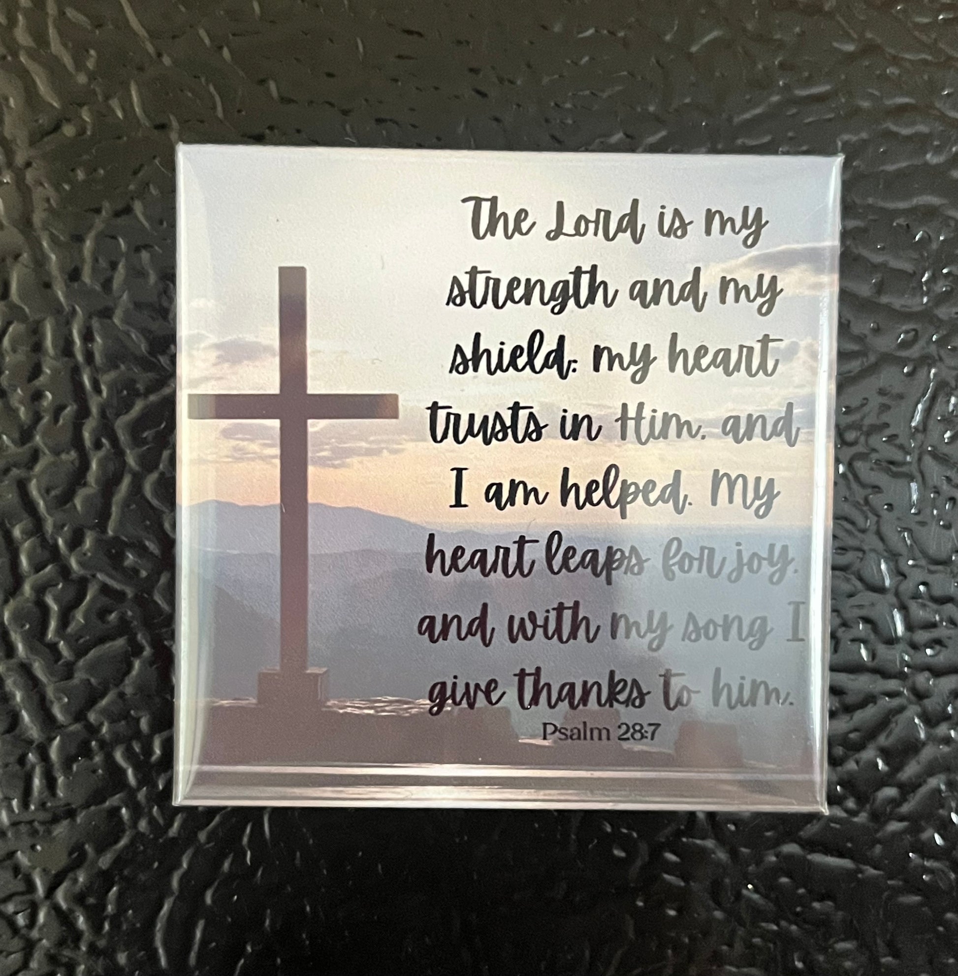 Psalms Scripture magnet on a fridge featuring a cross with mountains in the background and Psalm 28:7
