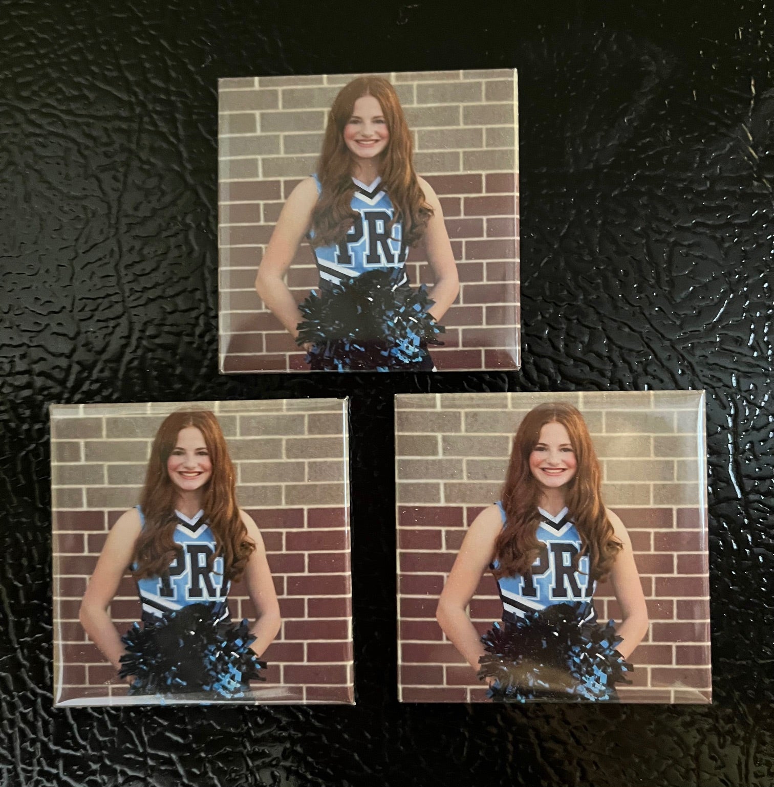 Set of 3 custom 2x2 photo magnets on a refrigerator displaying a 12-year-old's cheer photo
